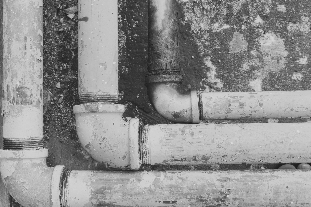 Old corroded plumbing pipes running across a weathered concrete wall