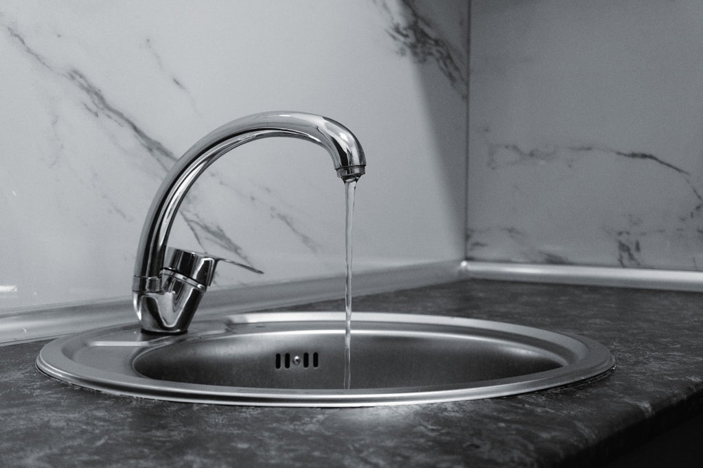 Chrome faucet with running water in a modern kitchen with marble countertop