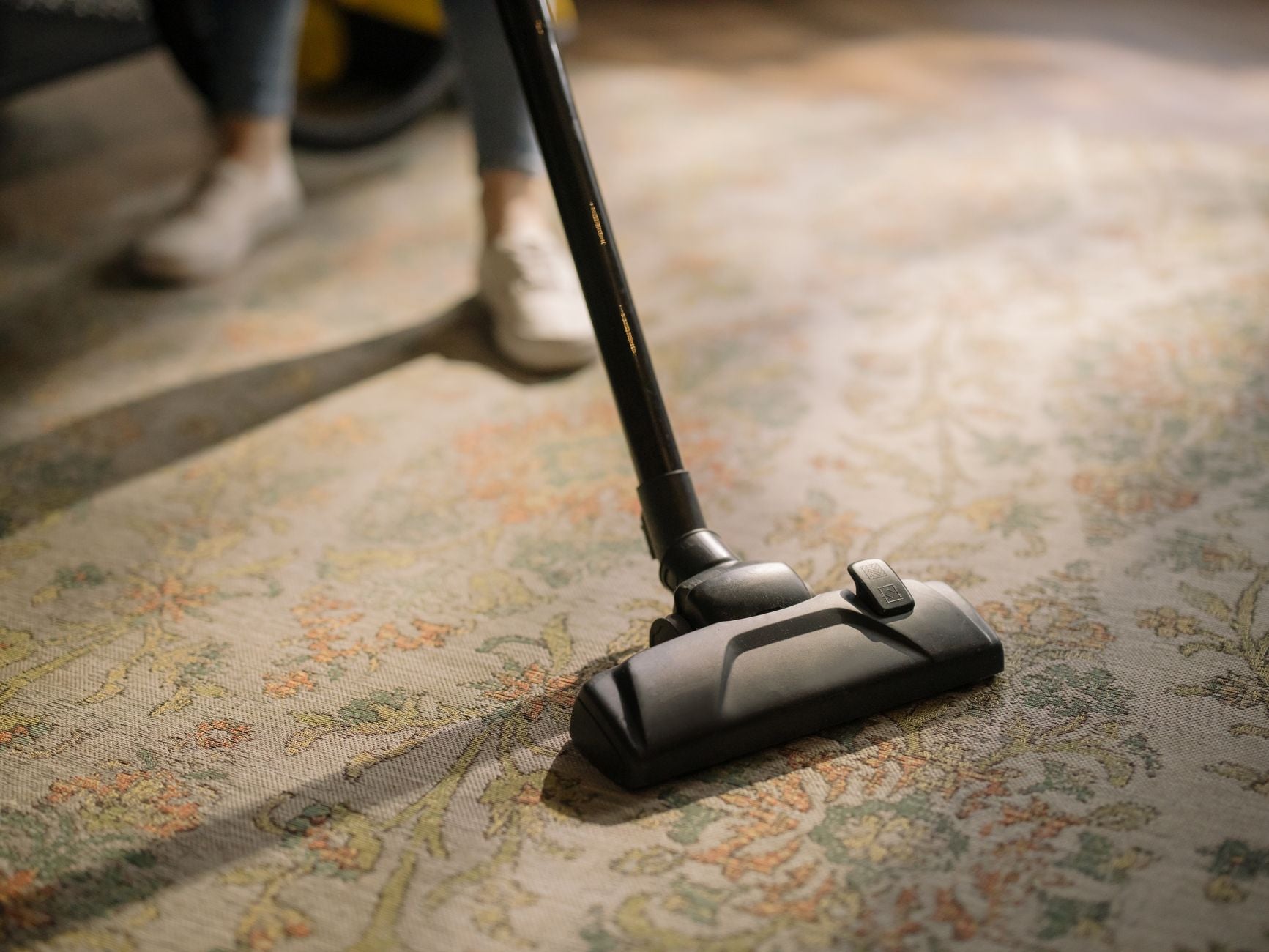 Close-up of a vacuum cleaner on a patterned carpet in a sunlit room, capturing a moment of household cleaning