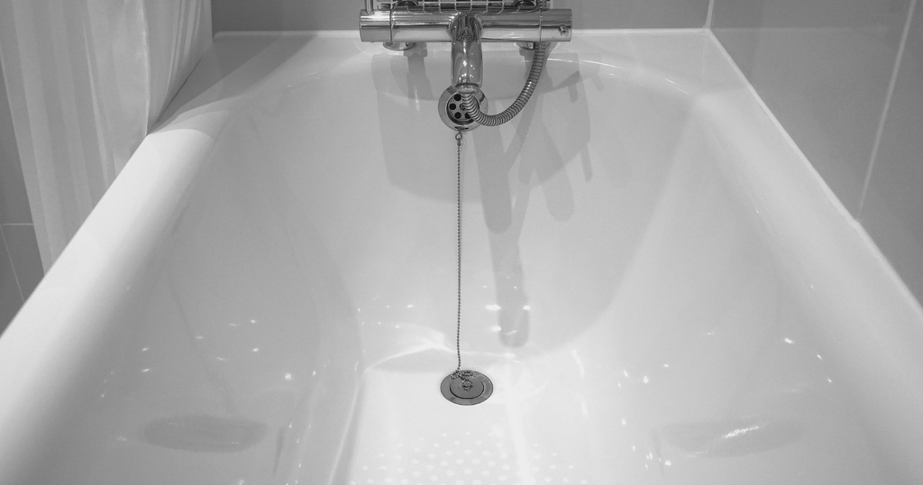 A clean white bathtub with a chrome drain and stopper chain