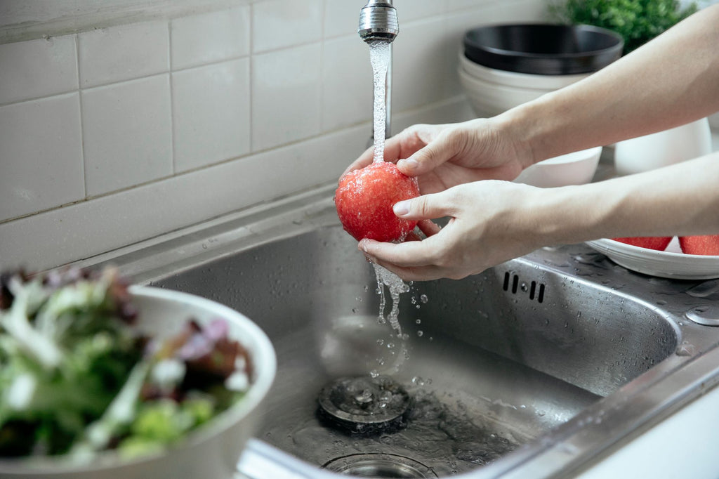 Hands washing a fresh red apple under running water at a kitchen sink